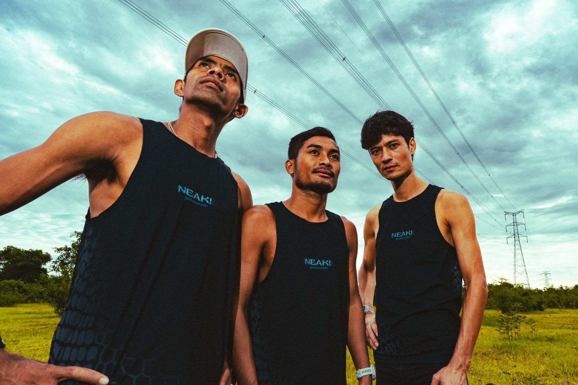 Three NEAK runners in Black Dragon singlets photographed from below against an open sky