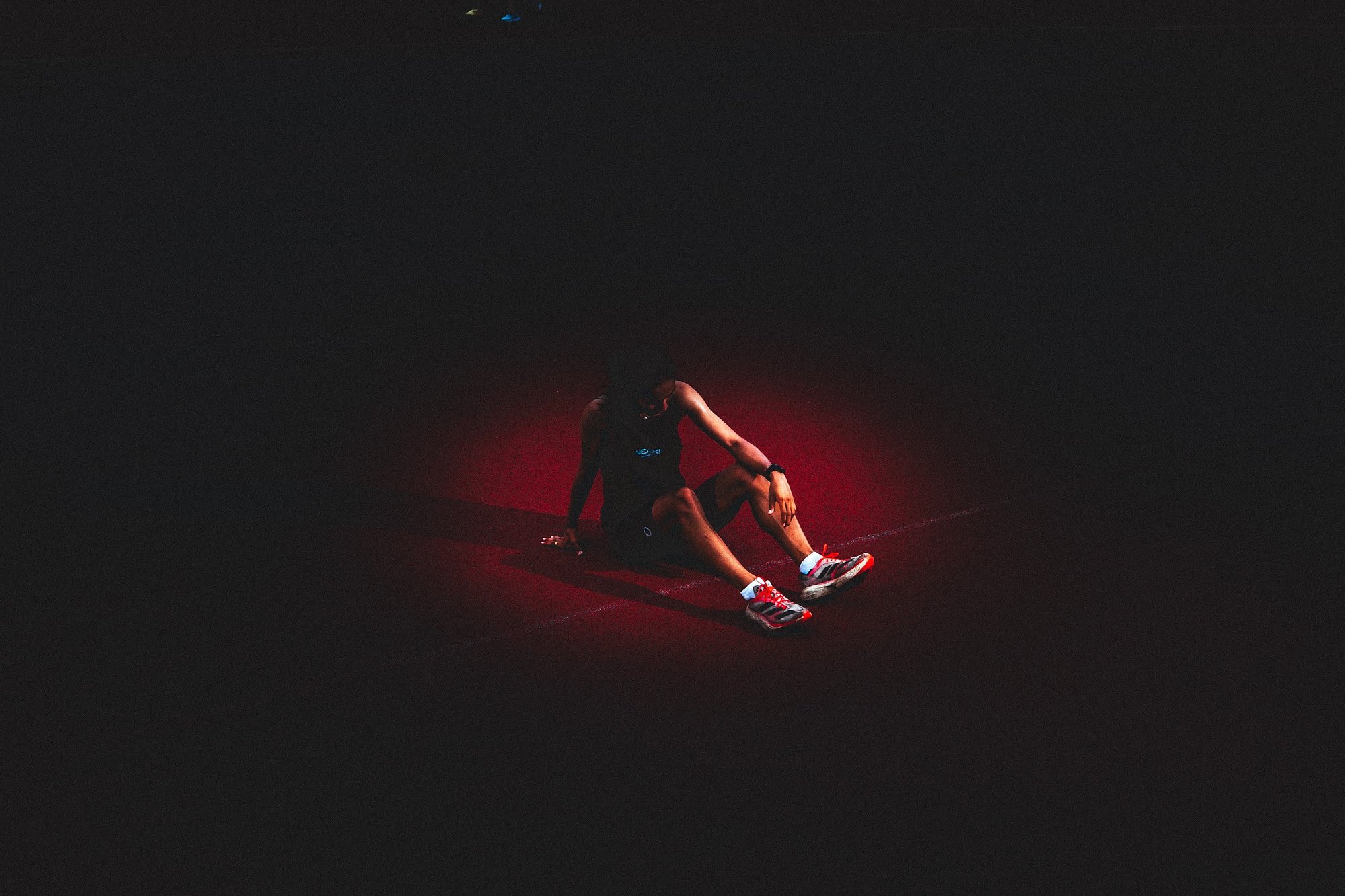 A single runner sitting on a floodlit red running track in near darkness